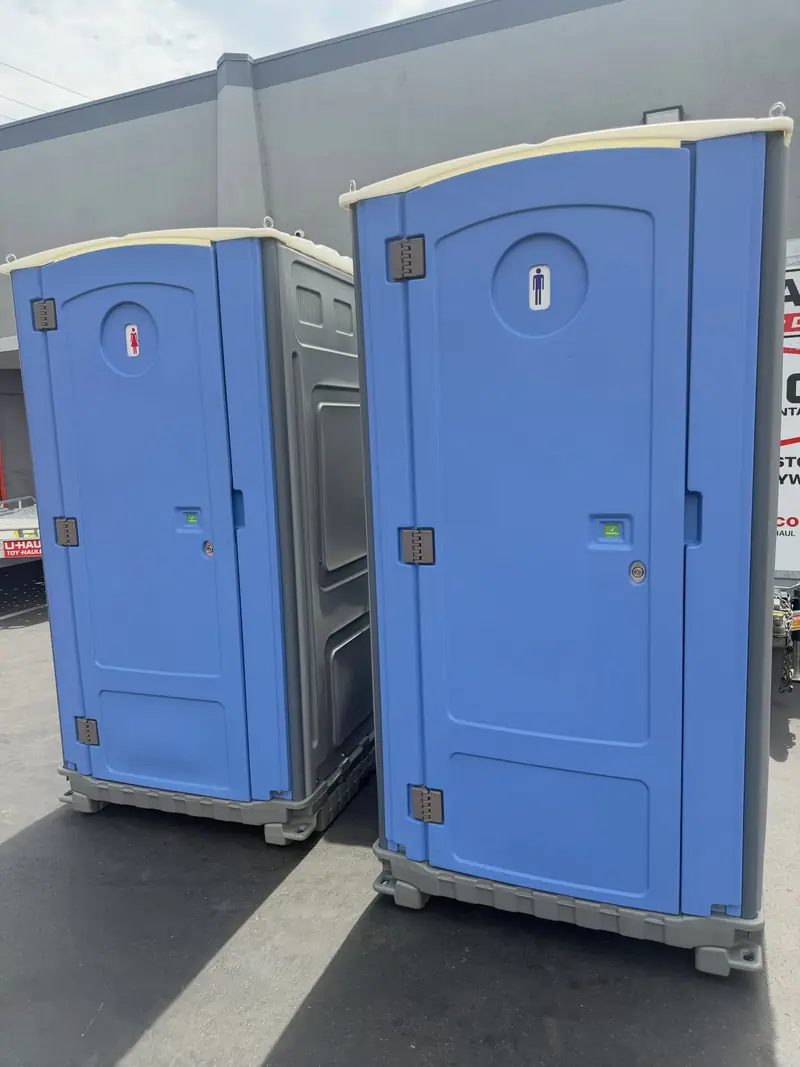 Two standard portable toilets side by side on pavement after same-day delivery